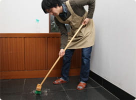 デッキブラシで玄関を洗う依藤。